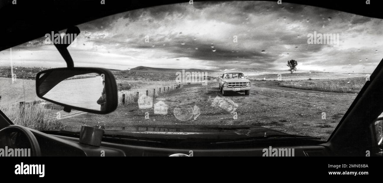 Vue sur le pare-brise d'une tempête de pluie approchant avec des personnes cherchant un abri à l'intérieur de leur voiture au barrage de Sheep Creek dans le comté de Grant, Dakota du Nord. Banque D'Images