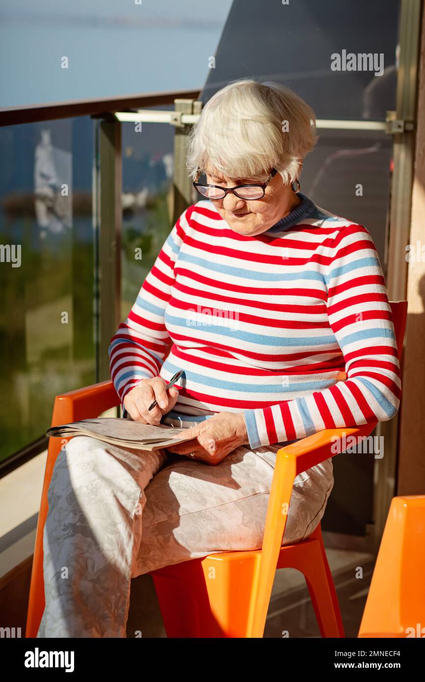 Femme âgée en lunettes, assise sur un balcon près de la mer Banque D'Images