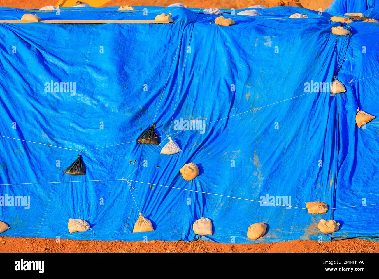 La grande bâche bleue maintenue par des sacs de sable couvre les matériaux à l'extérieur Banque D'Images