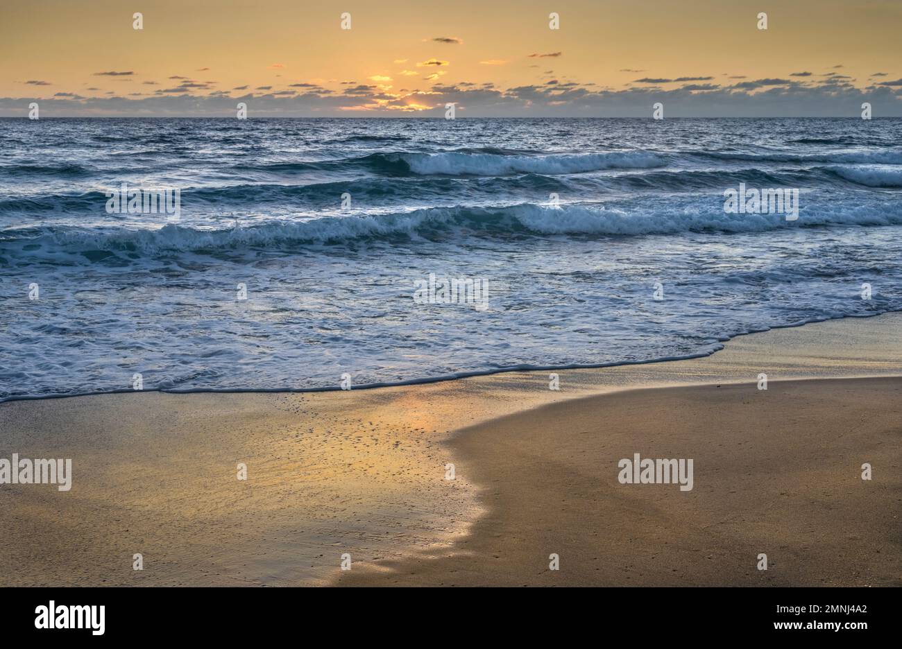 Plage de lavage des vagues de l'océan au coucher du soleil Banque D'Images