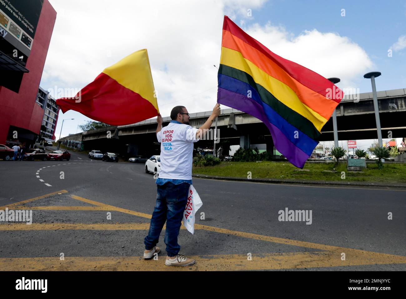 A supporter of presidential candidate Carlos Alvarado of the ruling Citizen Action Party waves a party banner and a rainbow banner to promote his candidate in San Jose, Costa Rica, Saturday, March 31, 2018. Voters will choose Sunday between Alvarado and Fabricio Alvarado of National Restoration. A recent poll indicated a statistical tie in the second-round runoff vote. (AP Photo/Arnulfo Franco) Banque D'Images