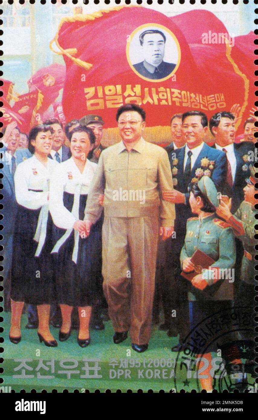 Timbre-poste nord-coréen de 2006 représentant Kim Jong-il et un portrait de Kim il-sung sur un drapeau rouge avec des citoyens. Banque D'Images