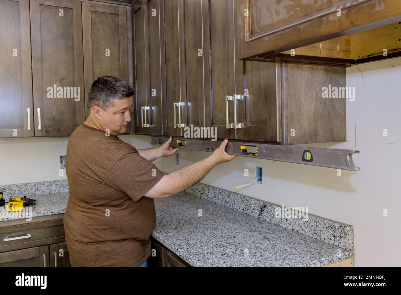 Installation de nouveaux meubles d'armoires de cuisine mis par un travailleur qui utilise le niveau pour le nivellement Banque D'Images