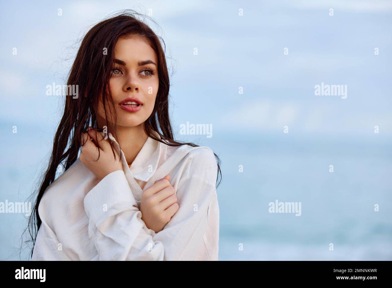 Portrait d'une belle femme pensive avec une peau bronzée dans une chemise de plage blanche avec des cheveux mouillés après avoir nagé sur la plage de l'océan coucher de soleil lumière avec Banque D'Images