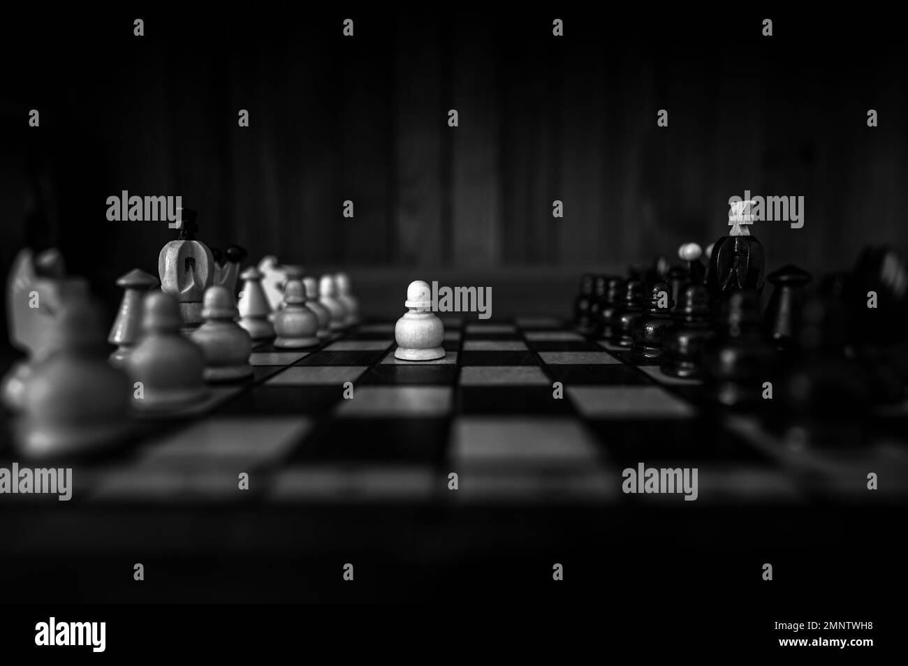 Arrière-plan noir et blanc flou avec une faible profondeur de mise au point. L'ensemble de pièces d'échecs en bois des éléments debout sur le plateau d'échecs sur fond sombre. Banque D'Images