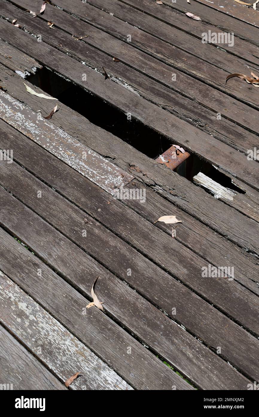 Planchers de terrasse en bois dangereux, pourris, non vernis, avec trous, espaces et feuilles sèches, dans un cadre extérieur Banque D'Images