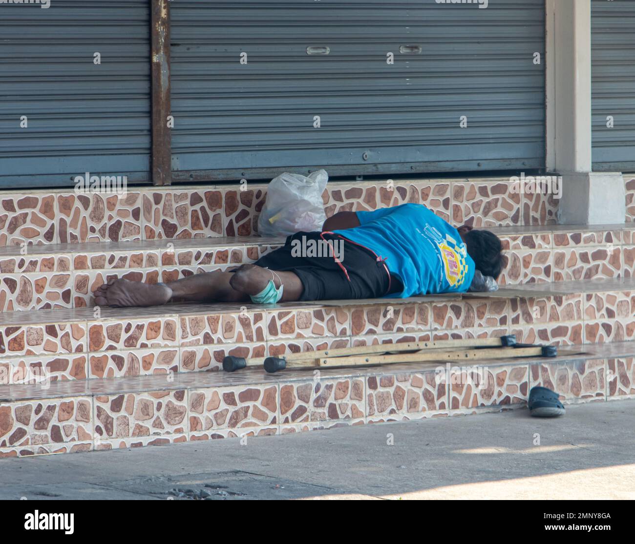 Homme handicapé - invalide, couché sur les escaliers devant la porte métallique fermée, Thaïlande 2023. Banque D'Images