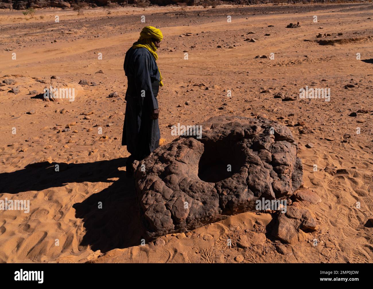 Tuareg homme en face d'un rocher pour stocker l'eau dans le désert, Parc national de Tassili n'Ajjer, Tadrar Rouge, Algérie Banque D'Images
