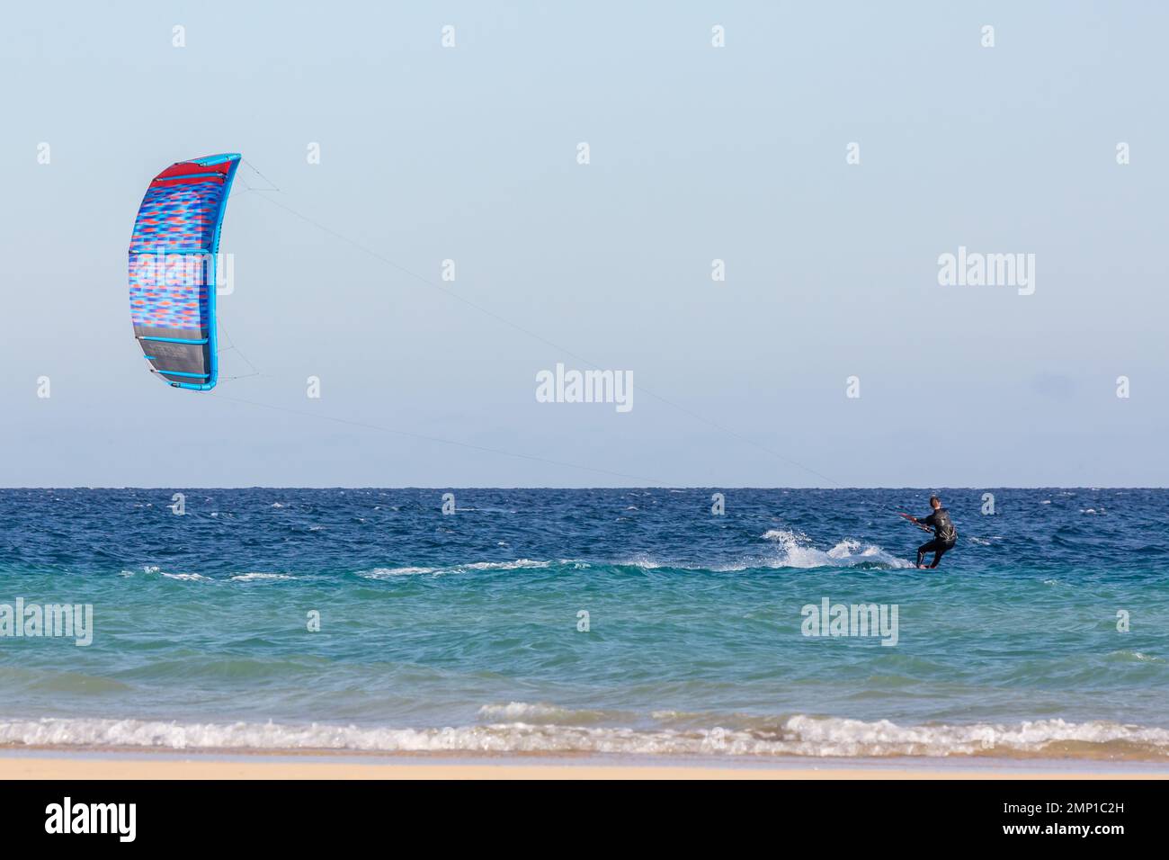 Kitesurfer glissant sur l'eau transportée par son cerf-volant bleu. Plage de Sotavento, Furteventura, îles Canaries. Banque D'Images