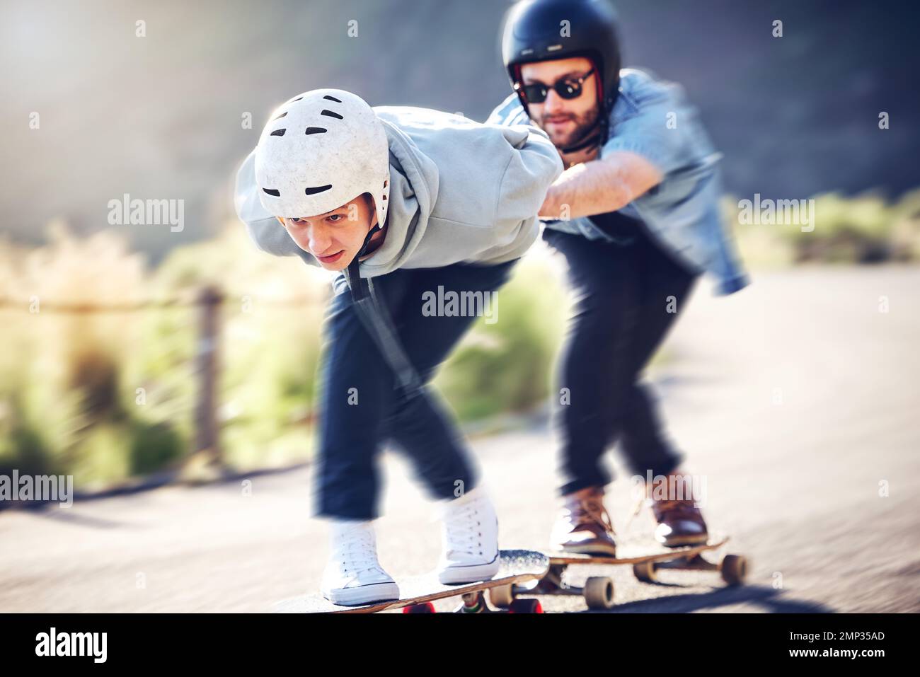 Patinage, longboard et amis qui voyagent rapidement sur une route, course en descente avec un skateboard et un casque pour plus de sécurité. Sports extrêmes, vitesse et personnes ou Banque D'Images