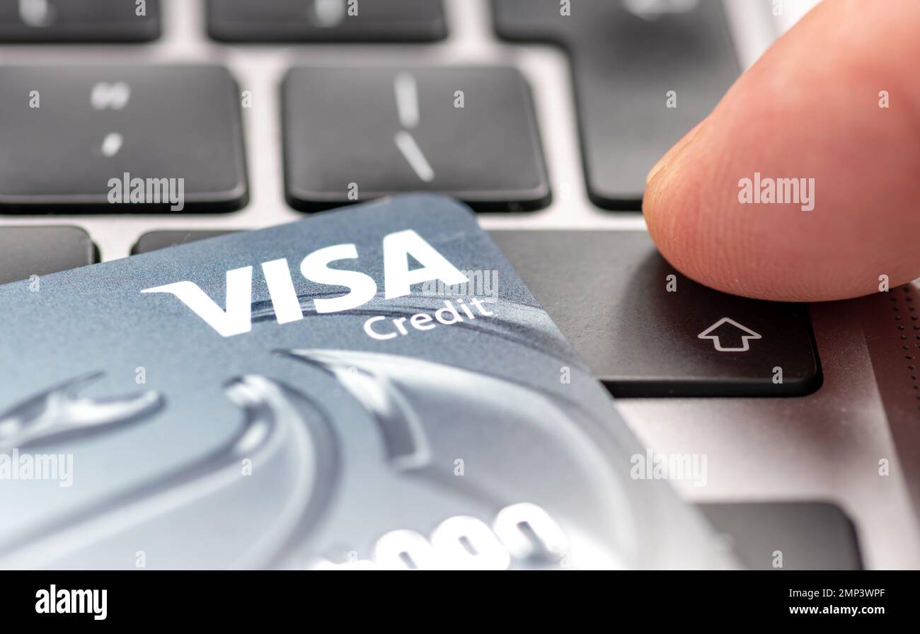 Londres. ROYAUME-UNI- 01.29.2023. Une carte de crédit Visa au-dessus d'un ordinateur portable avec une personne qui appuie sur le bouton ENTER. Banque D'Images