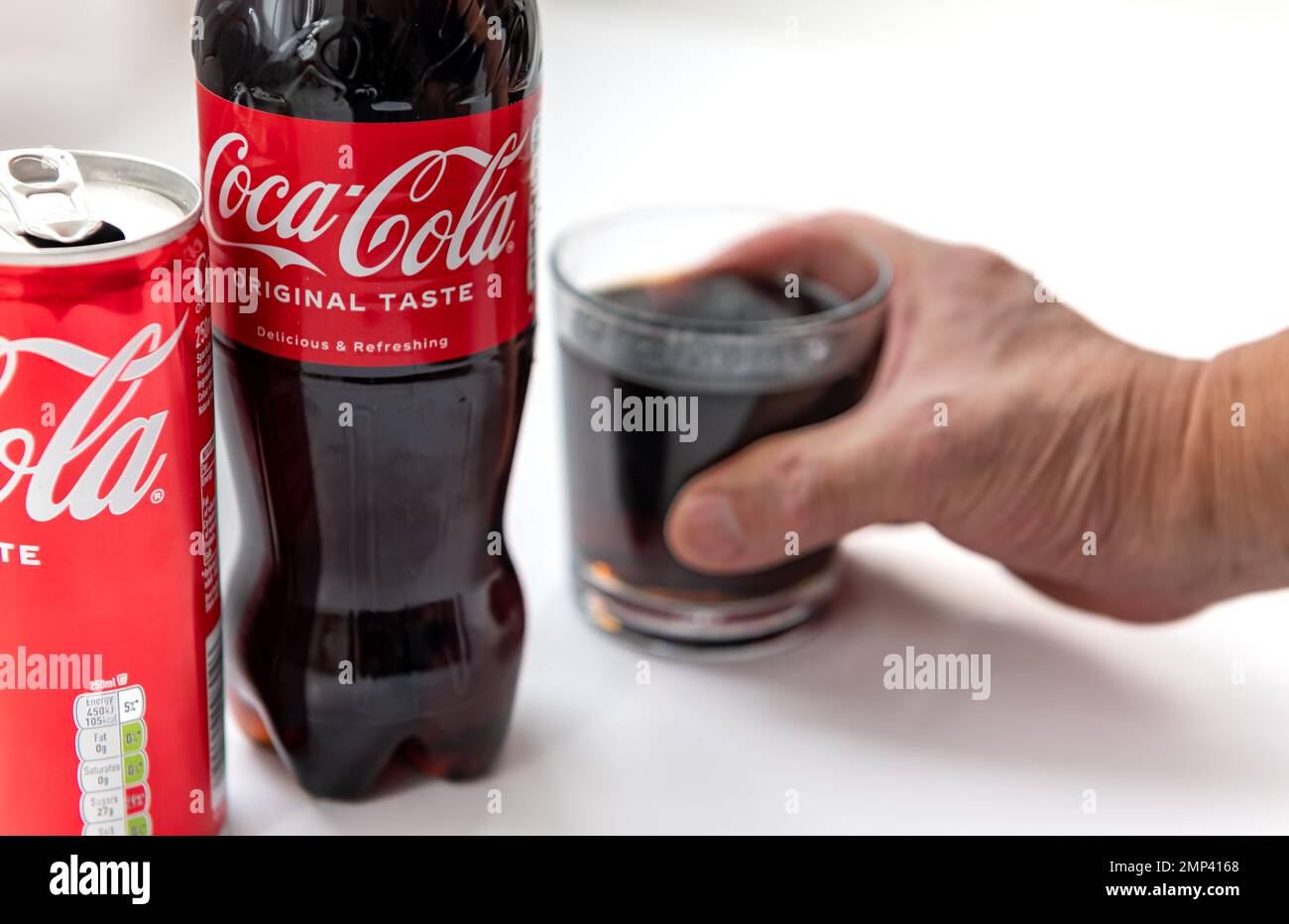 Londres. ROYAUME-UNI- 01.29.2023. Une bouteille et une boîte de Coca Cola goût original isolé en blanc avec une personne cueillant un verre de la boisson. Banque D'Images