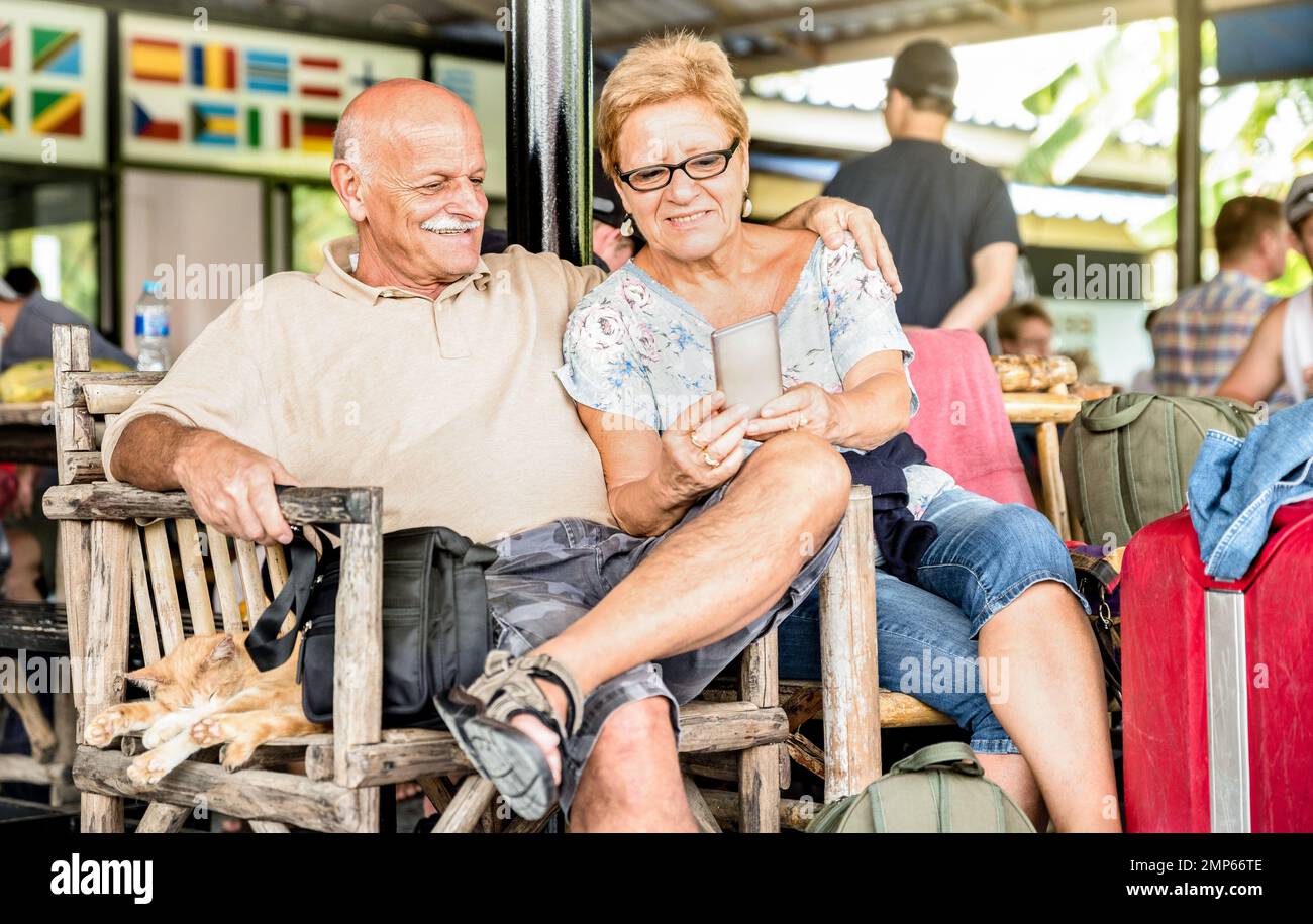 Couple senior heureux assis et utilisant un smartphone mobile avec une valise de voyage lors d'un voyage aventure dans le monde entier - Active de style de vie de personnes âgées concep Banque D'Images