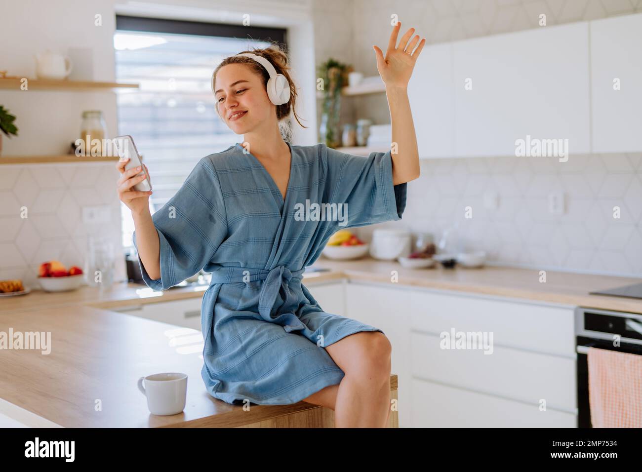 Jeune femme écoutant de la musique et prenant une tasse de café le matin, dans sa cuisine. Banque D'Images