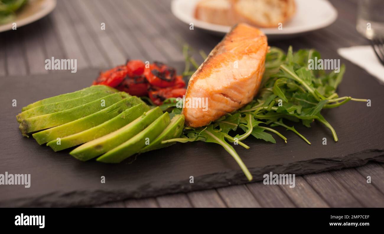 plat de filet de saumon cuit avec légumes frais et herbes sur une assiette en pierre noire Banque D'Images