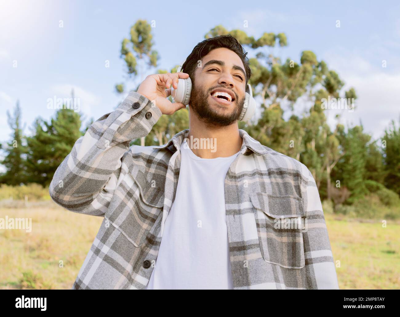 Musique, heureux et l'homme se détendre dans un parc, sourire et rire au podcast ou piste audio sur fond de nature. Écouteurs, rire et gars beau Banque D'Images