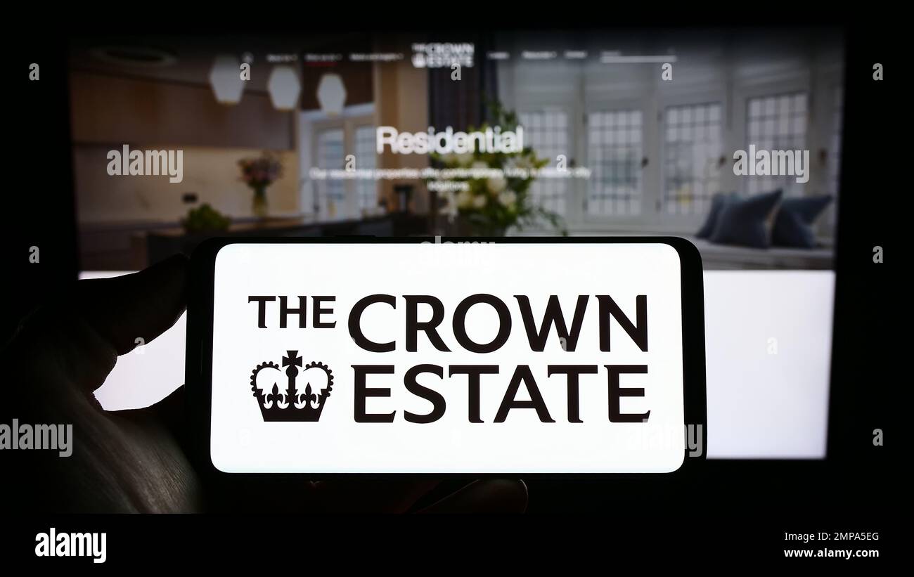 Personne tenant un téléphone cellulaire avec le logo de la société statutaire britannique Crown Estate sur l'écran devant la page Web d'affaires. Mise au point sur l'affichage du téléphone. Banque D'Images