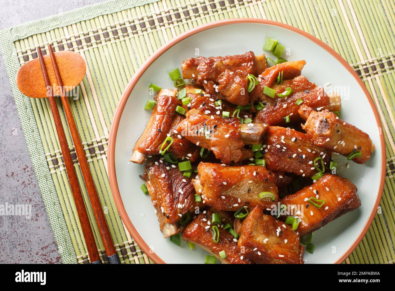 Côtelettes sucrées et aigres chinoises avec oignon vert et sésame gros plan dans une assiette sur la table. Vue horizontale du dessus Banque D'Images