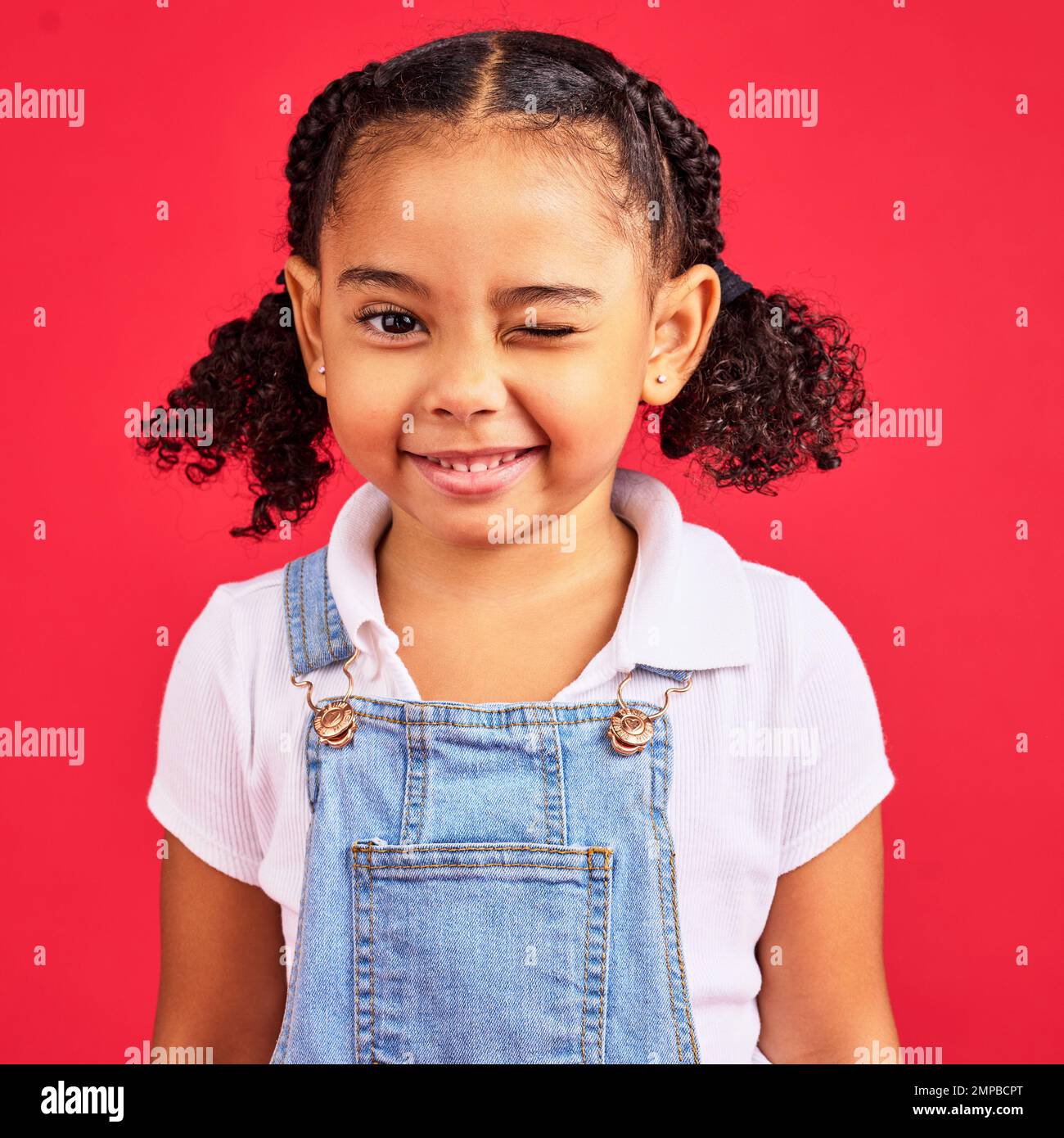Portrait, clin d'œil et enfant noir sur fond rouge en studio, amusant ou insouciant. Enfants, mode et sourire avec une femme heureuse enfant Banque D'Images