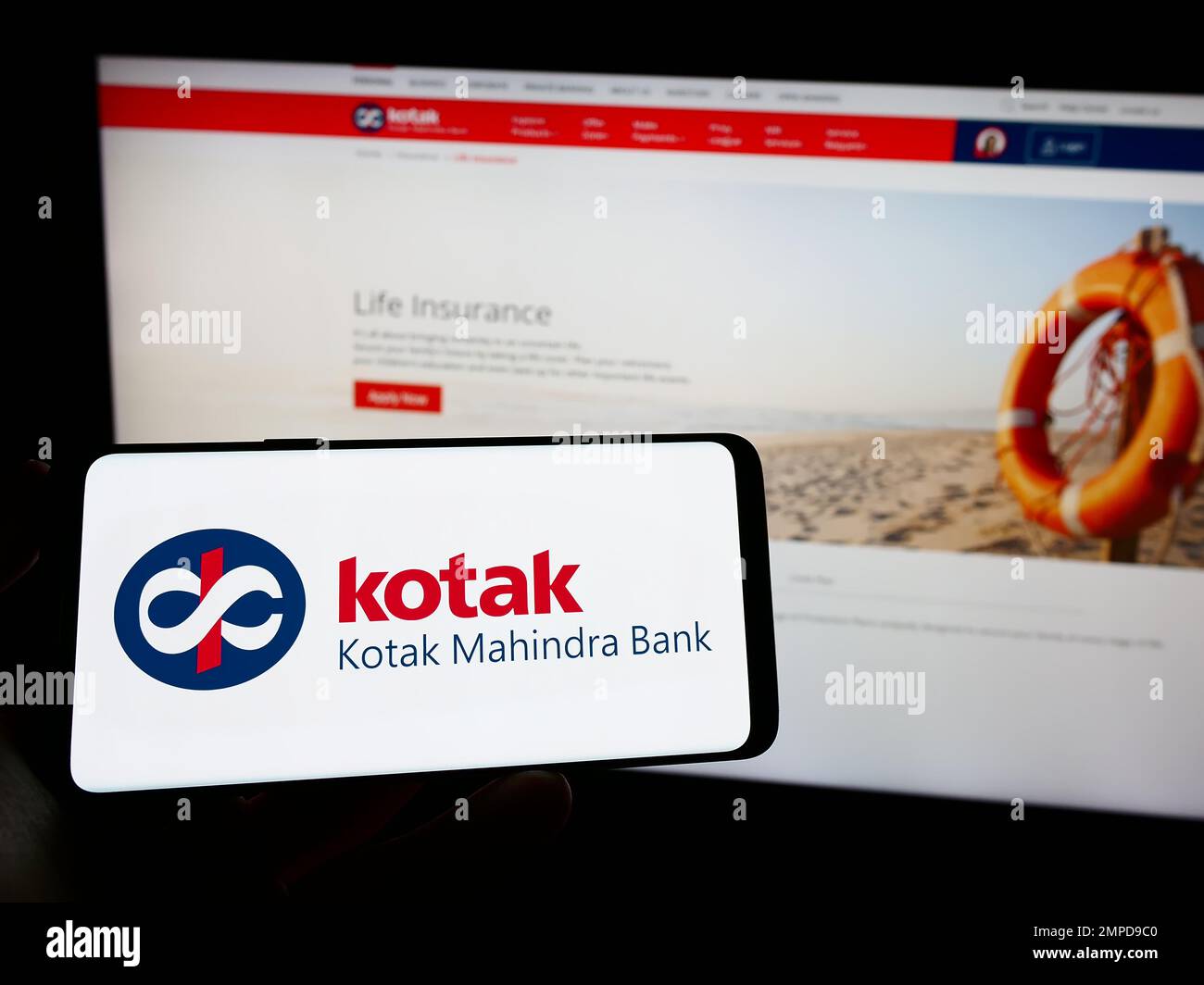 Personne tenant le téléphone portable avec le logo de la société financière indienne Kotak Mahindra Bank sur l'écran en face de la page web d'affaires. Mise au point sur l'affichage du téléphone. Banque D'Images