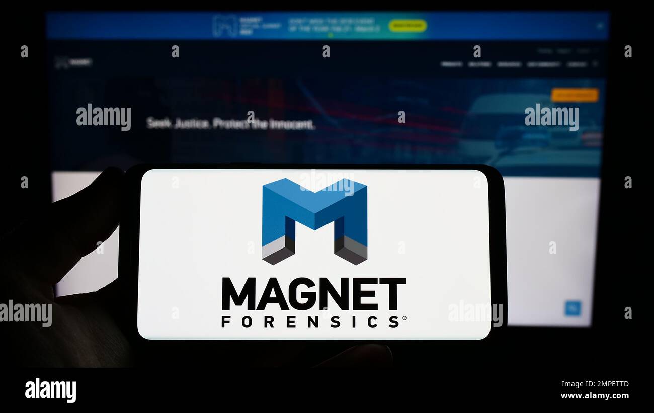 Personne tenant un smartphone avec le logo de la société de cybersécurité Magnet Forensics Inc. À l'écran devant le site Web. Mise au point sur l'affichage du téléphone. Banque D'Images