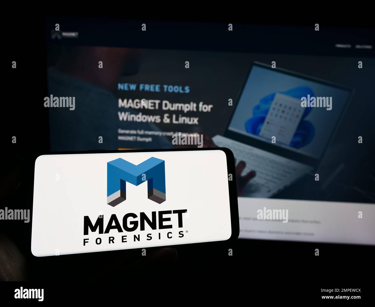 Personne tenant un téléphone portable avec le logo de la société de  cybersécurité Magnet Forensics Inc. À l'écran en face de la page Web  d'affaires. Mise au point sur l'affichage du téléphone