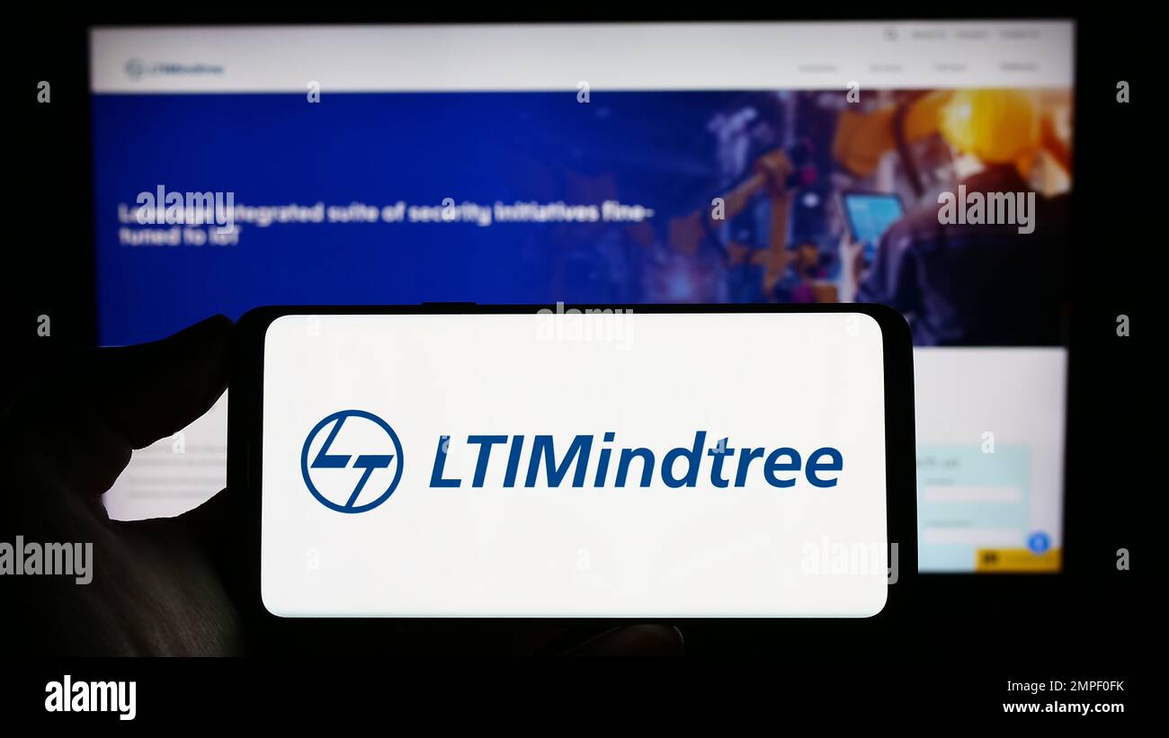 Personne tenant un téléphone mobile avec le logo de la société indienne DE TI LTIMIDTree Limited à l'écran devant la page Web d'affaires. Mise au point sur l'affichage du téléphone. Banque D'Images