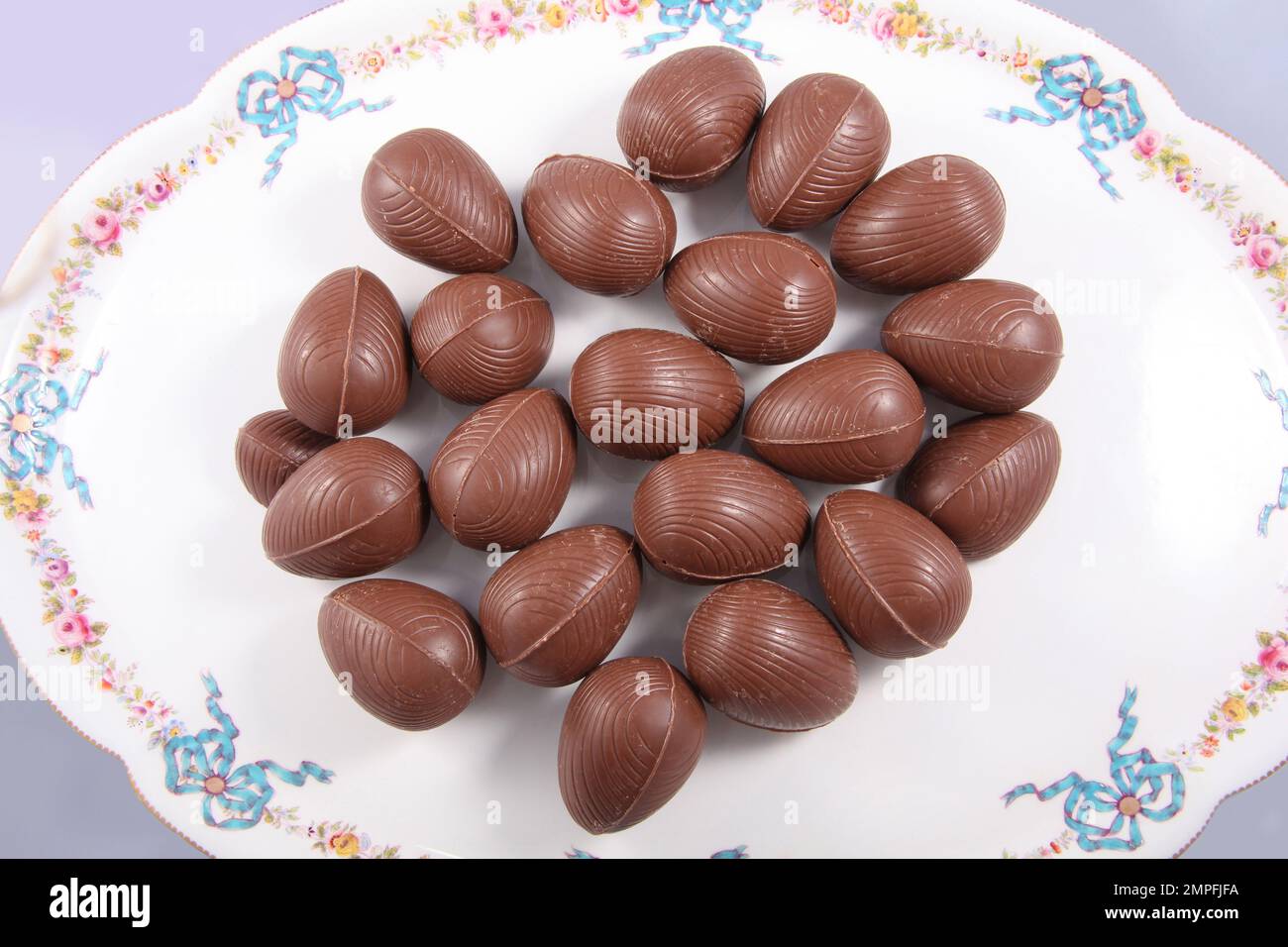 Groupe d'oeufs de Pâques au chocolat sur une assiette blanche avec des décorations traditionnelles de noeuds et de fleurs et un fond pâle. Banque D'Images