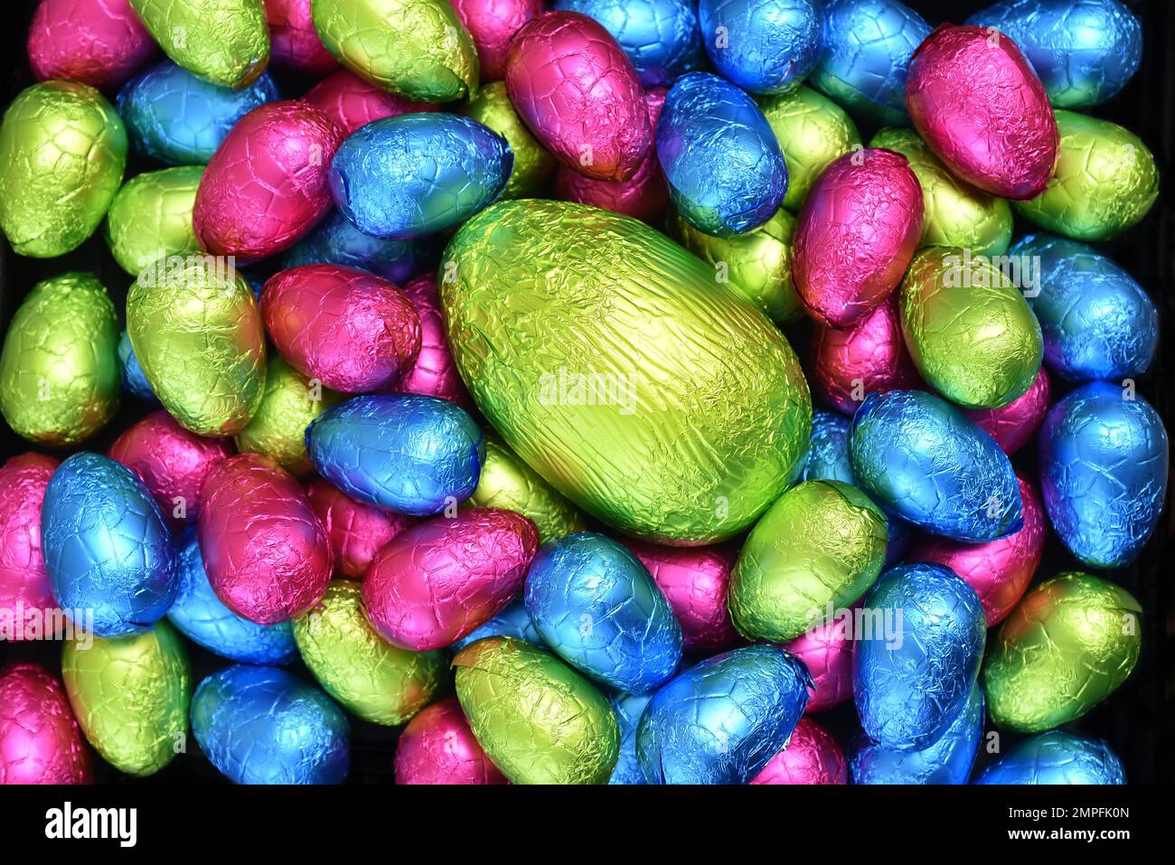 Pile ou groupe de plusieurs couleurs et différentes tailles d'oeufs de pâques au chocolat enveloppés d'une feuille colorée en rose, bleu, jaune et vert lime. Banque D'Images