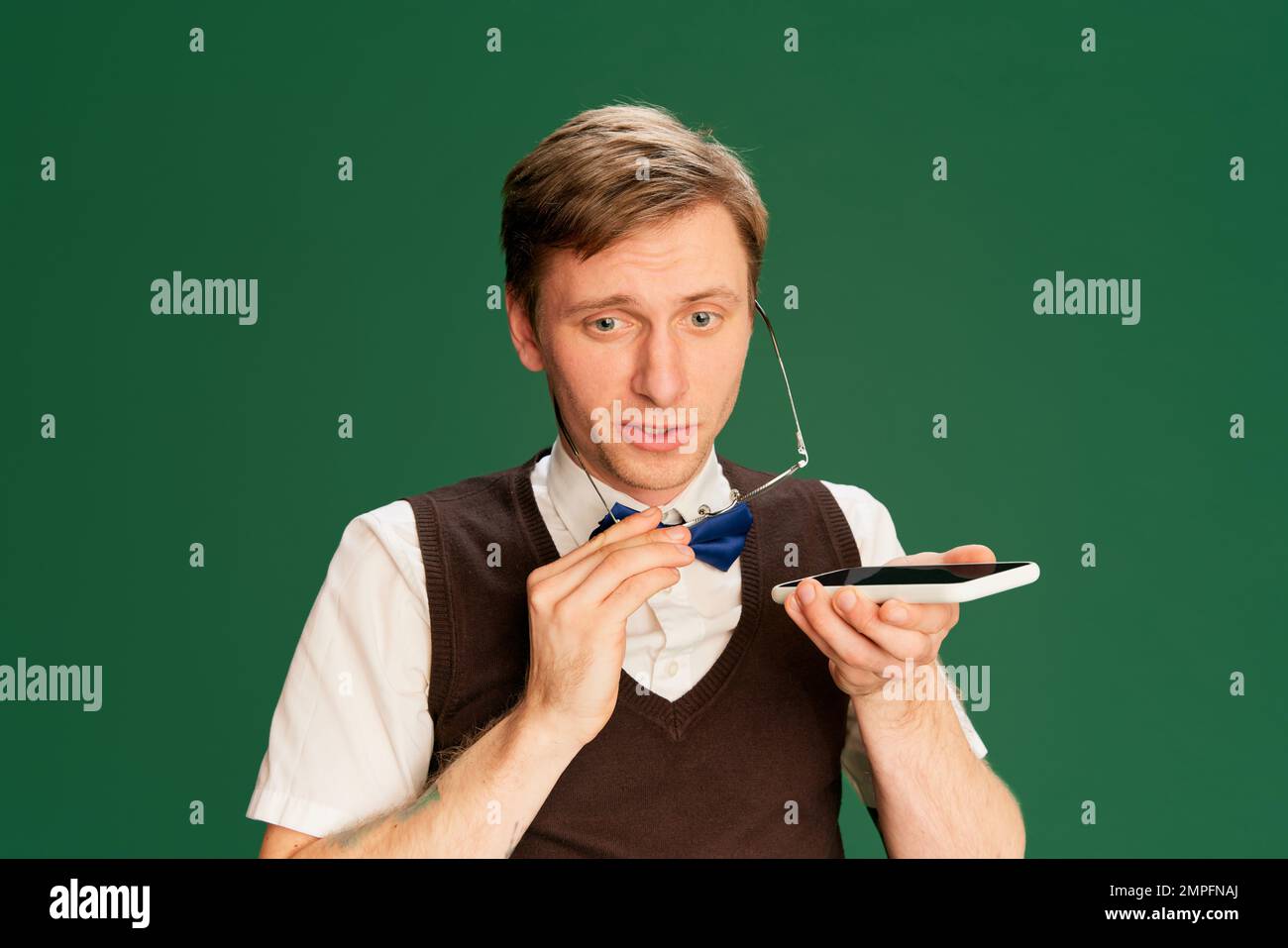 Haut-parleur. Parler au téléphone. Portrait de l'homme dans des vêtements classiques élégants, short et gilet posé sur fond vert studio. Concept des émotions Banque D'Images