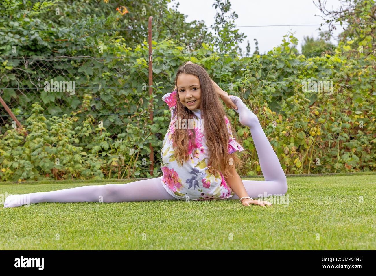 Flexible fille à cheveux longs effectue des exercices de gymnastique dans le jardin. Horizontalement. Banque D'Images