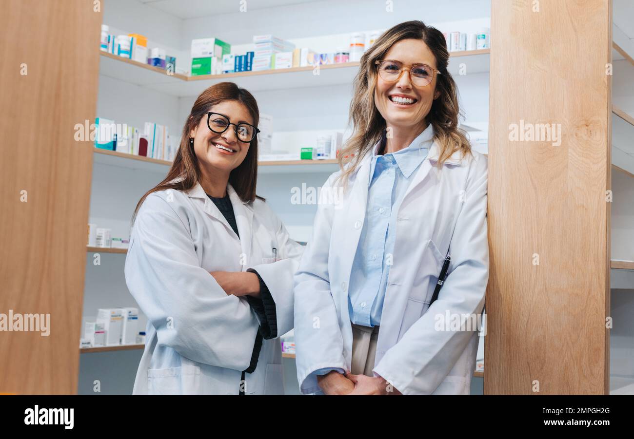 Femmes pharmaciens debout dans un chimiste et souriant à l'appareil photo. Deux professionnels de la santé travaillant ensemble dans une pharmacie. Banque D'Images