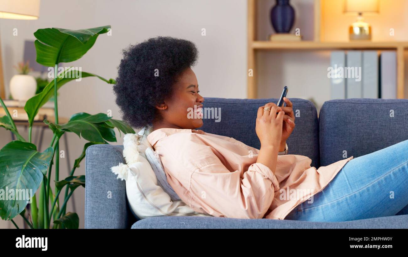 Une jeune femme qui rit envoie un SMS sur un téléphone à la maison. Une femme joyeuse bavarde avec ses amis sur les réseaux sociaux, navigue en ligne et regarde drôle Banque D'Images