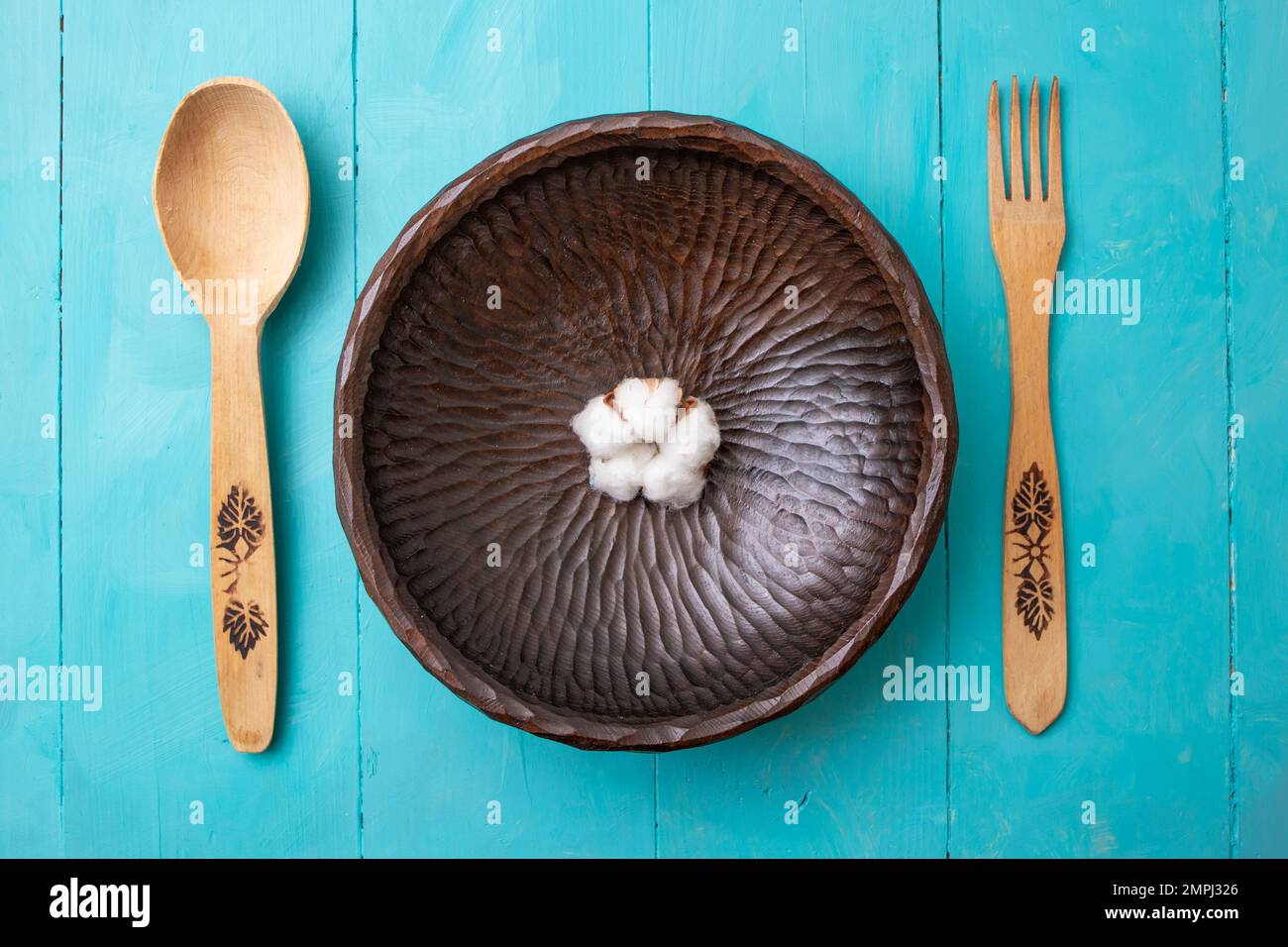 Fourchette en bois, cuillère et bol sculpté avec une fleur de coton, sur fond de tableaux peints en bleu acrylique. Banque D'Images