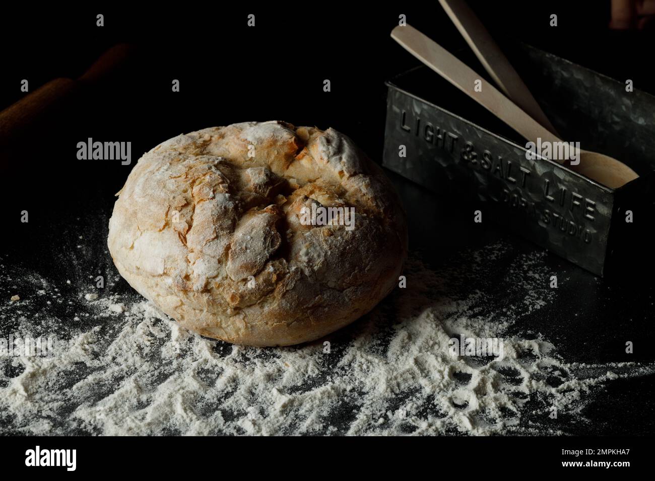 Pain de pain maison traditionnel fraîchement cuit, avec de la farine et une boîte d'aluminium sur fond sombre. Pain artisanal de levain de seigle, pain de wholegrain. Clos Banque D'Images