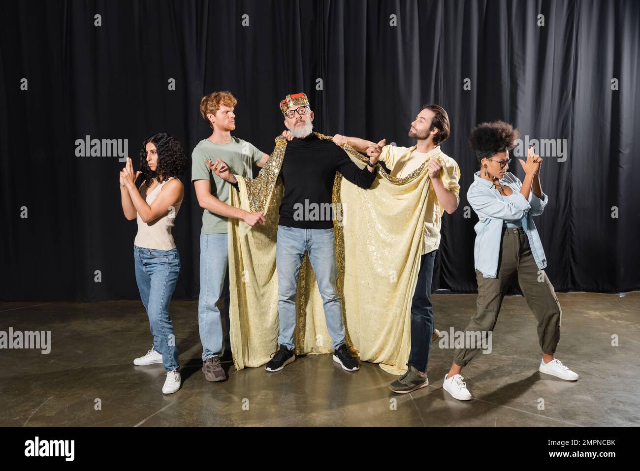 directeur artistique barbu debout en costume de roi près d'étudiants multiculturels jouant des gardes sur scène dans le théâtre Banque D'Images