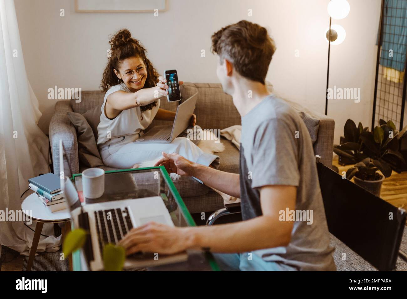 Bonne petite amie montrant un smartphone à un ami avec un ordinateur portable à la maison Banque D'Images