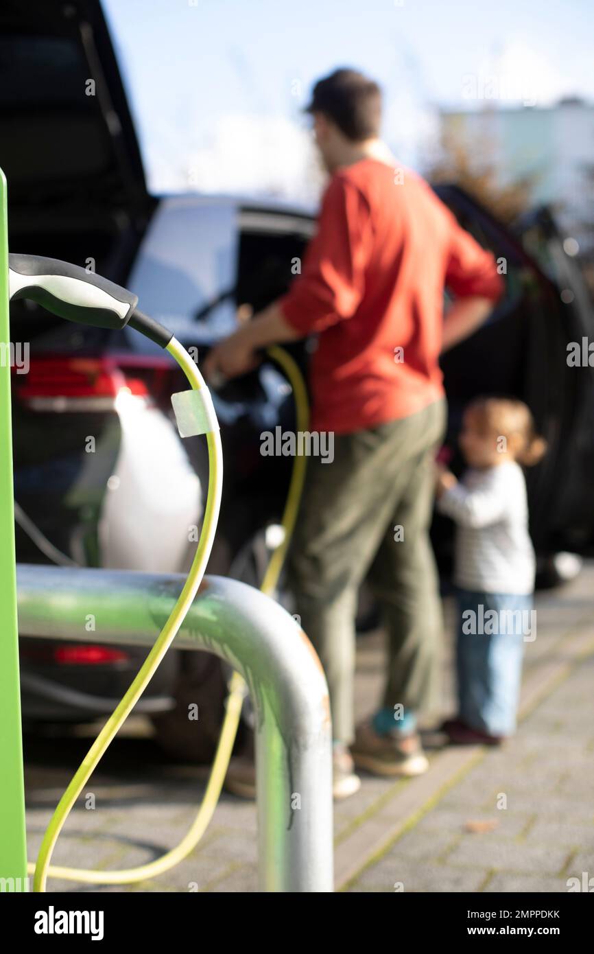 Câble branché à la station avec un homme qui charge la voiture électrique en arrière-plan Banque D'Images