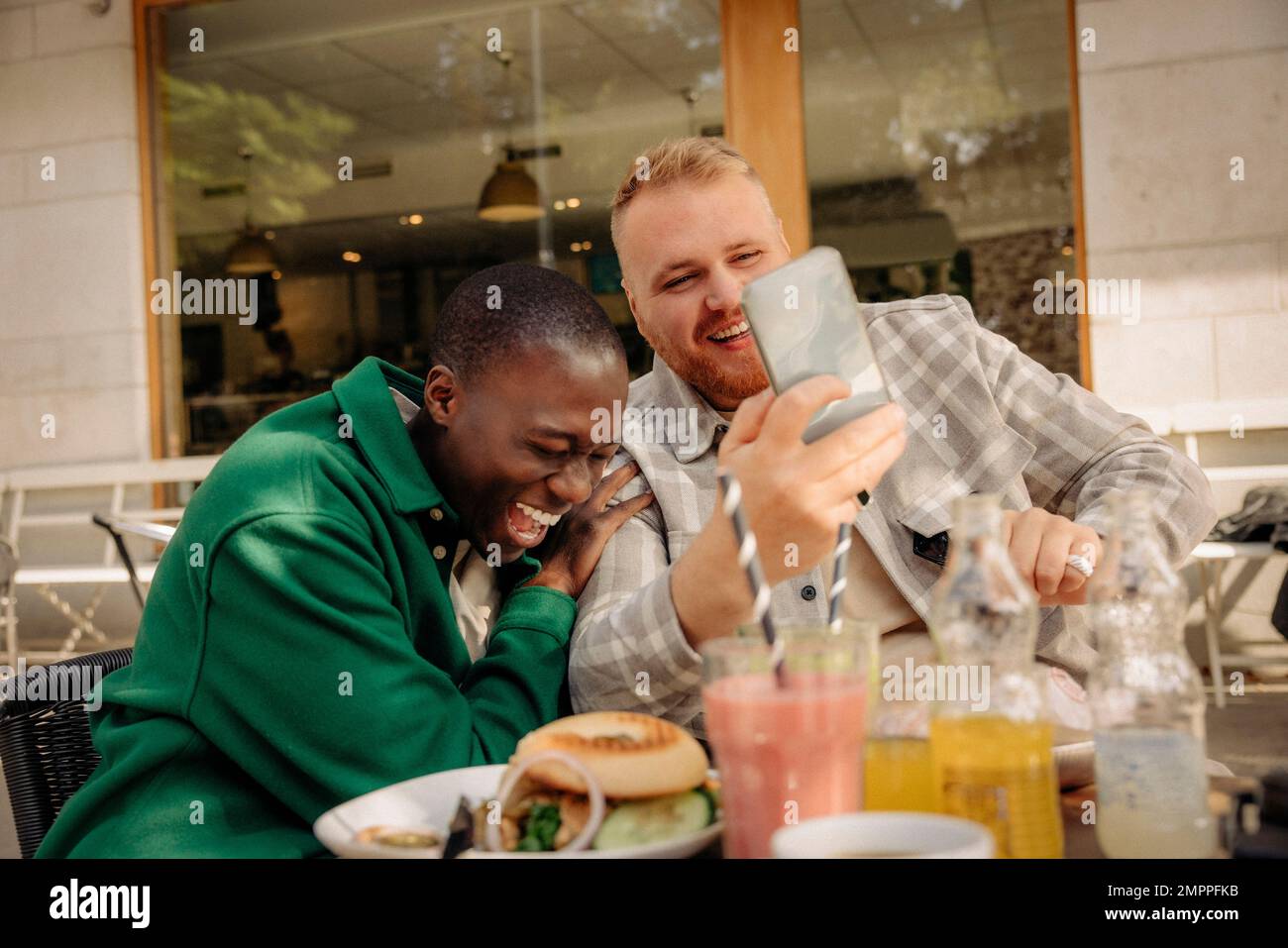 Homme souriant partageant un téléphone intelligent avec un ami masculin heureux lorsqu'il est assis au café-terrasse Banque D'Images