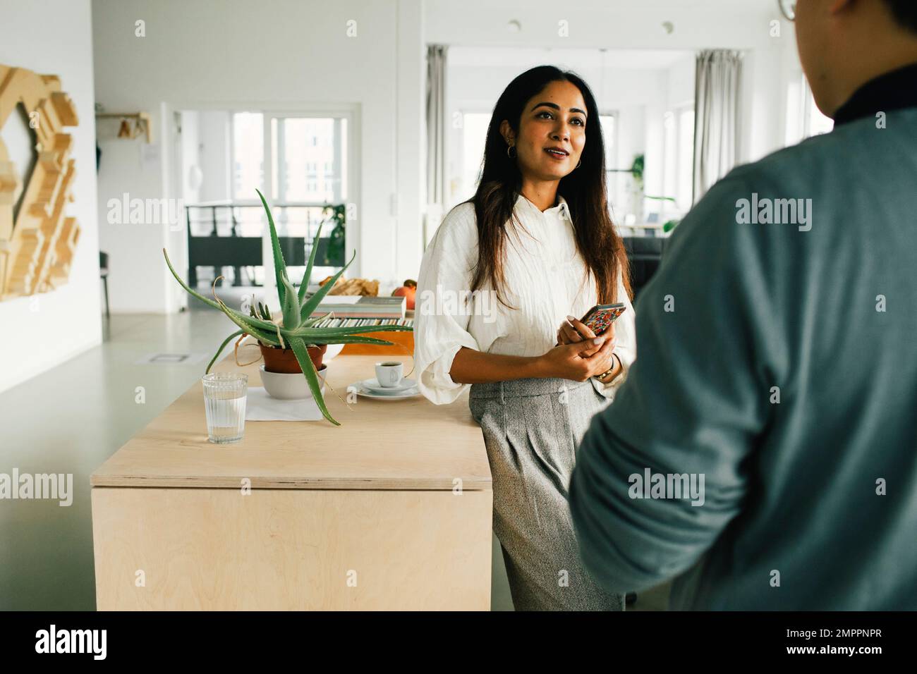 Femme d'affaires parlant à un collègue pendant qu'elle se penche sur une table au bureau Banque D'Images
