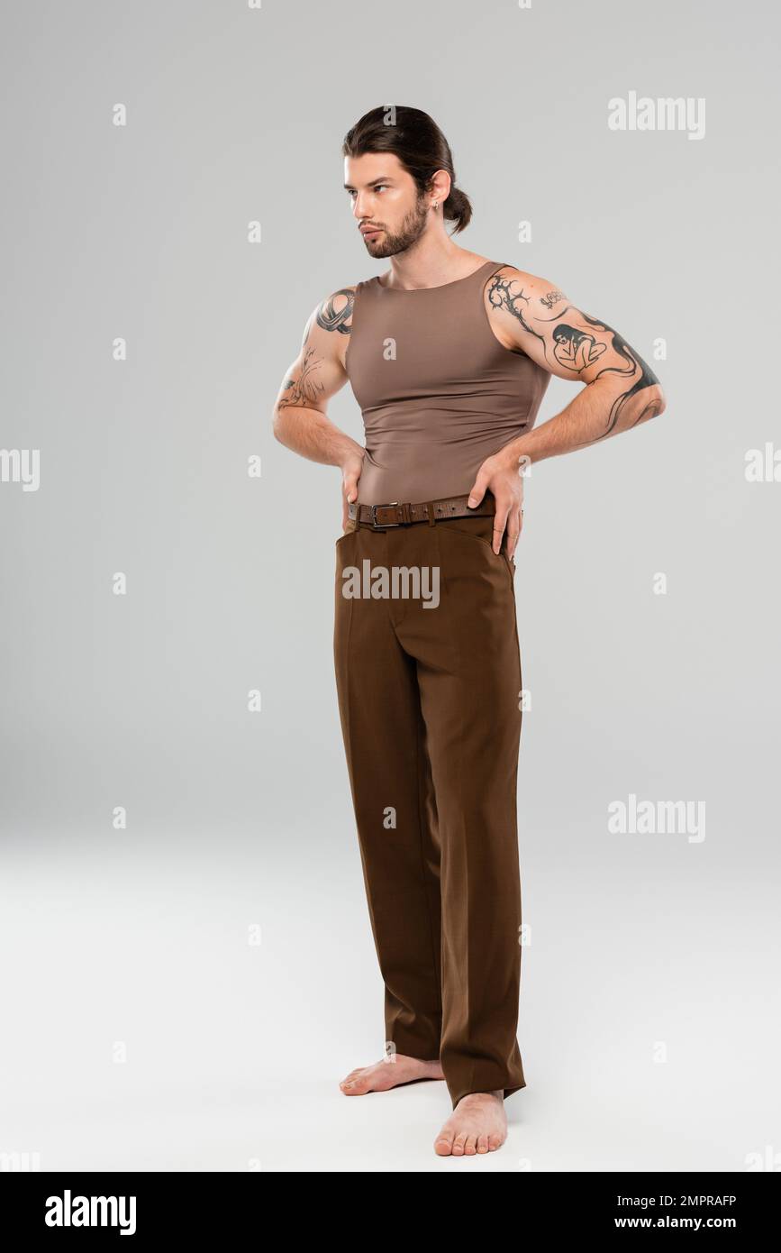 Pieds nus et tatoués homme dans le pantalon et débardeur posant sur fond gris Banque D'Images