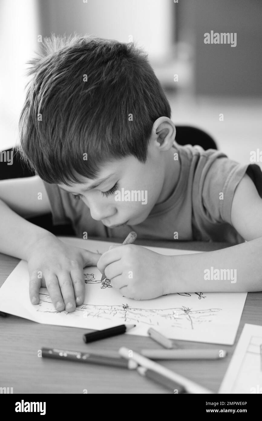 Un garçon caucasien assis par une table et coloriage Winnie l'Ourson pages Banque D'Images