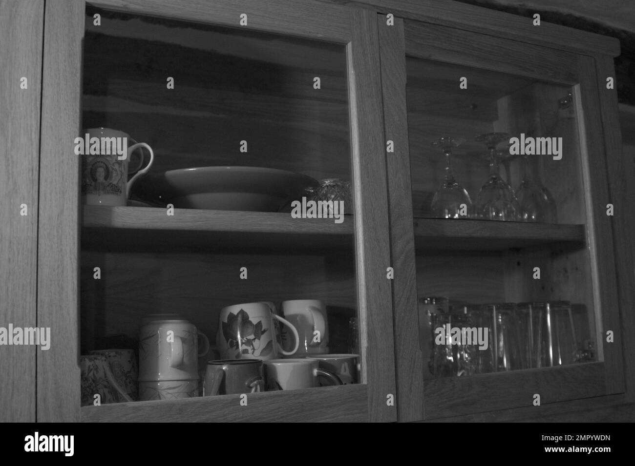 Photo noir et blanc d'un meuble de cuisine en bois avec verre montrant des verres à boire, des verres à vin, des mugs, des tasses et une assiette Banque D'Images