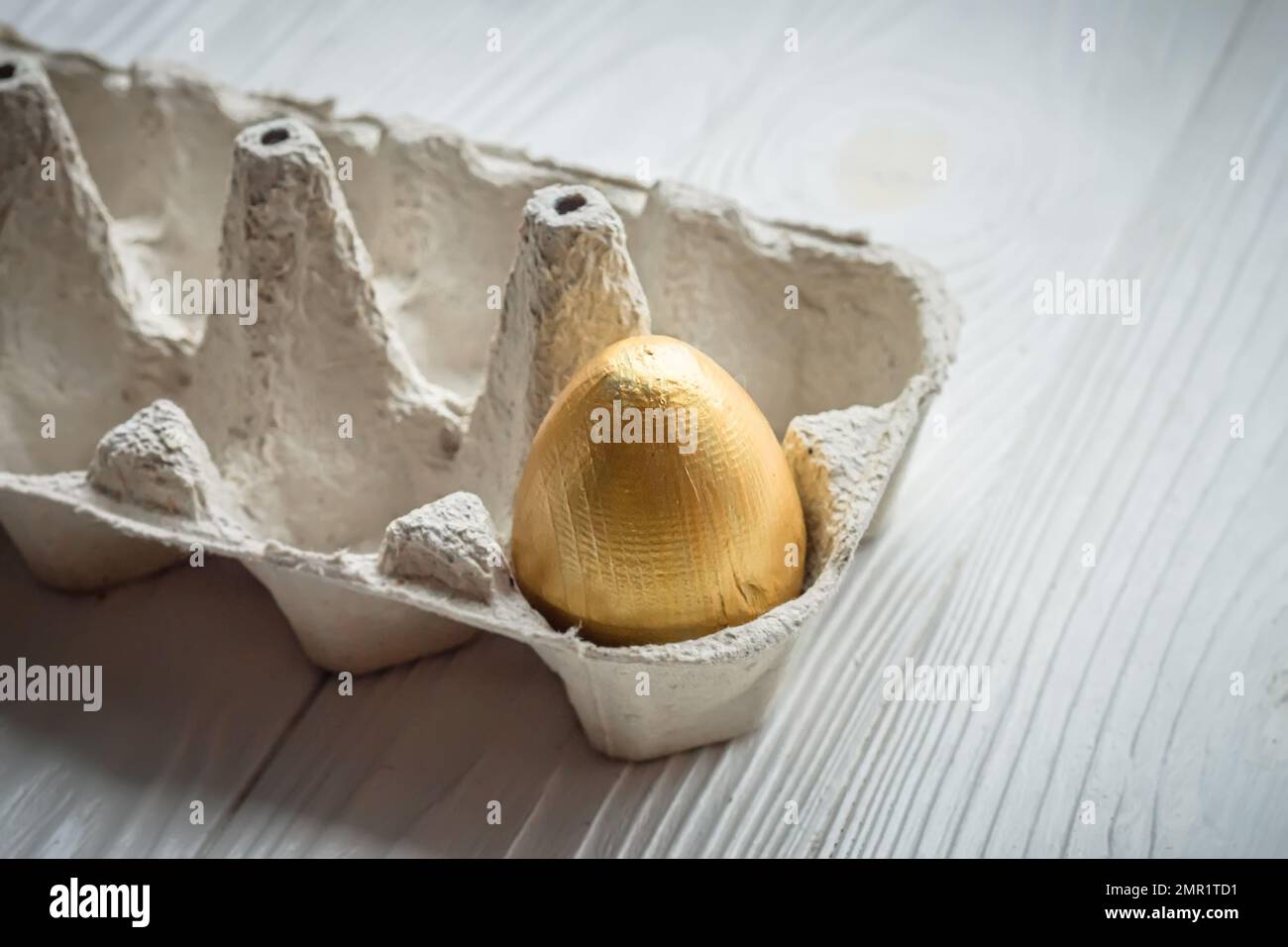 Œuf doré dans un plateau en carton ordinaire Le concept d'une vie riche. Œufs de Pâques dans une boîte à œufs Banque D'Images