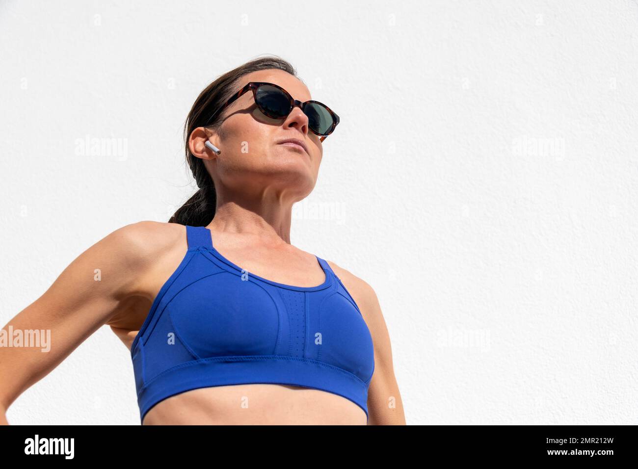 Gros plan sur une femme sportive d'un âge adulte moyen portant des écouteurs sans fil pendant son entraînement au soleil Banque D'Images