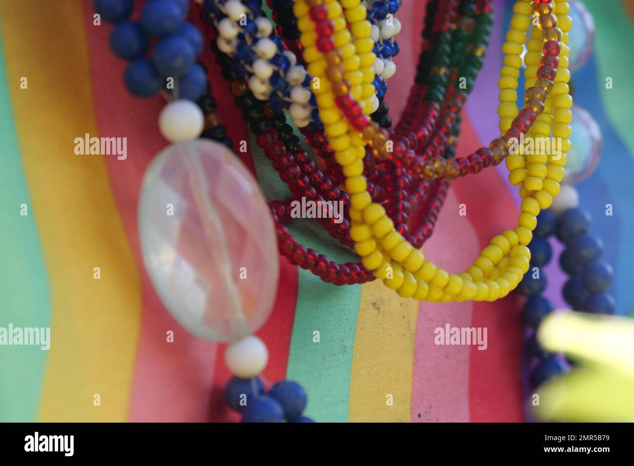 Gros plan de perles de verre colorées accrochées devant un matériau coloré. Arrière-plan partiellement flou ou flou Banque D'Images