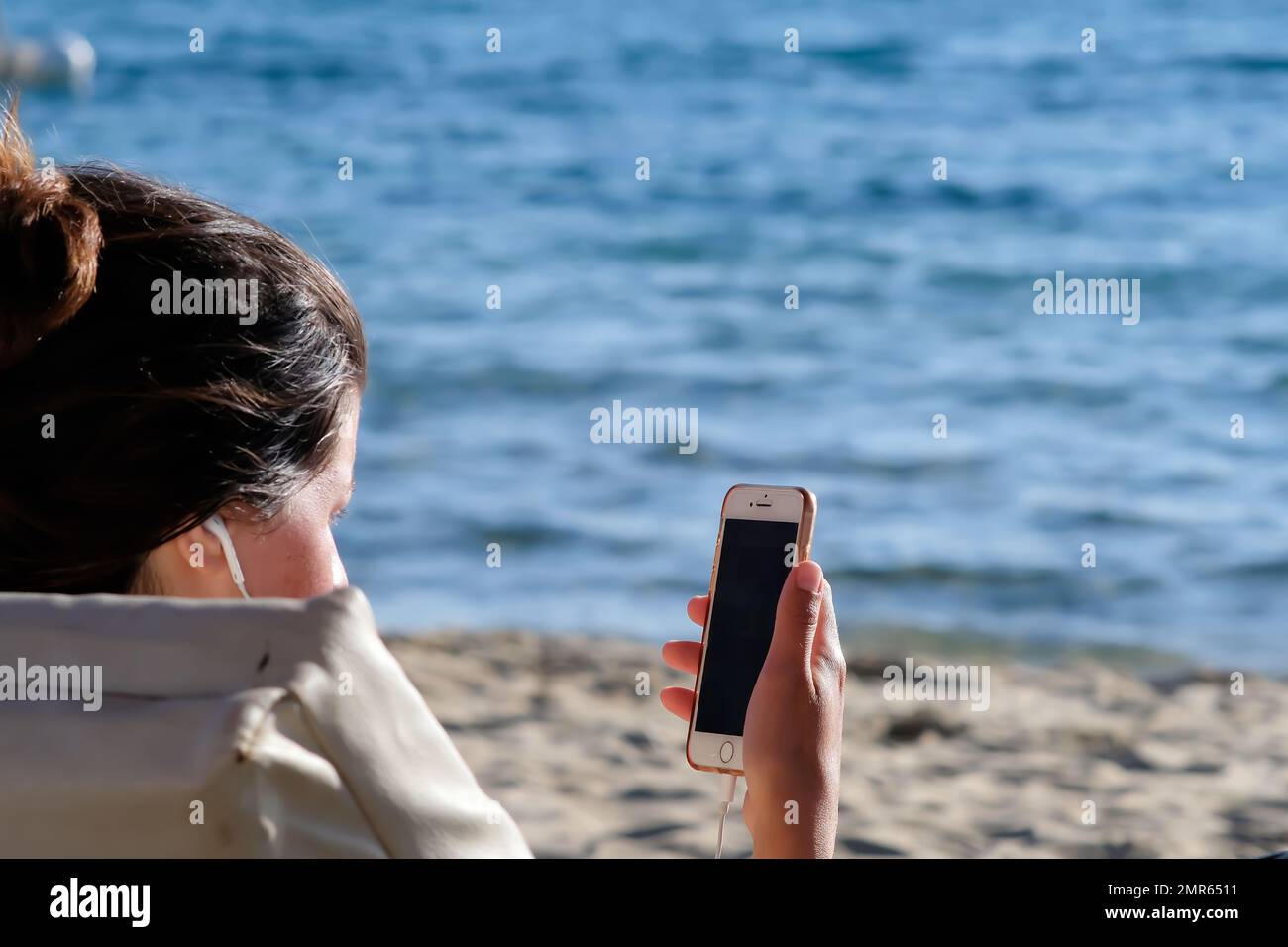 Vue d'une jeune femme à la plage à l'aide de son téléphone portable et de ses écouteurs dans iOS Grèce Banque D'Images