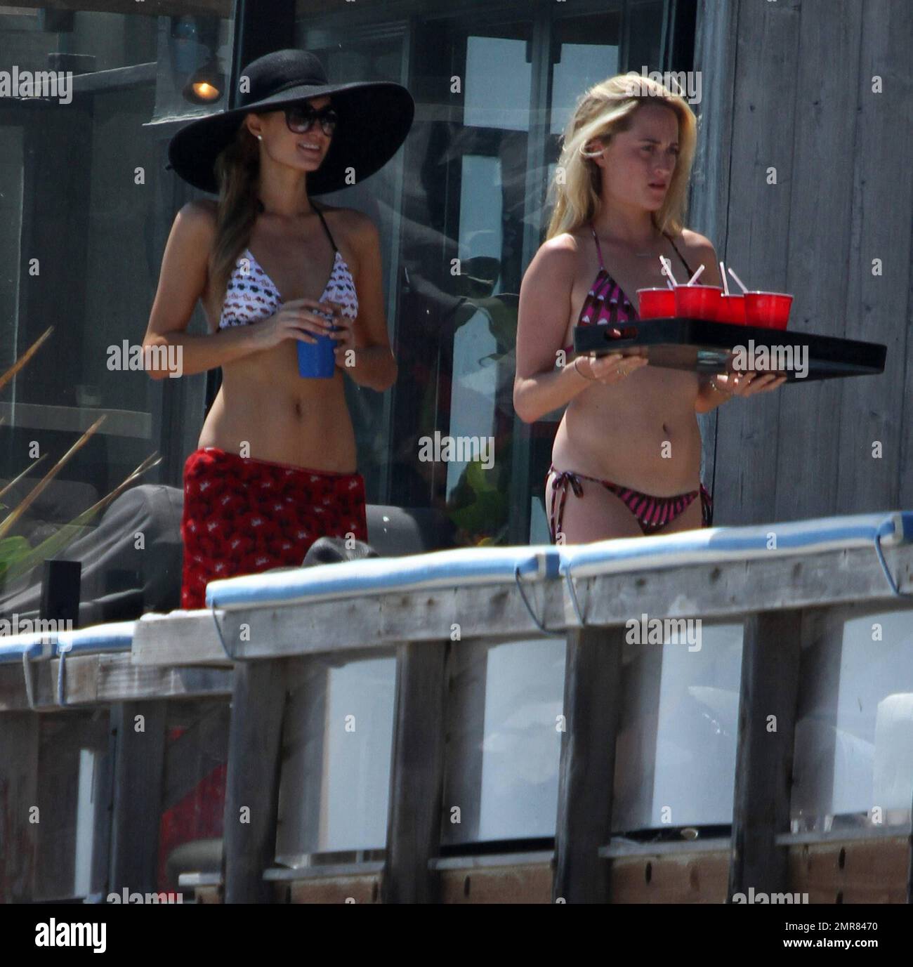 Les sœurs Hilton, Paris et Nicky sont repérées en appréciant le week-end de vacances dans leur maison de plage Malibu. Paris portait une robe rouge vif qu'elle tira pour dévoiler un bikini blanc à motif lunettes de soleil lorsqu'elle posa sur le balcon en prenant des photos avec son iPhone. Nicky portait une robe d'été verte. Malibu, Californie 6 juillet 2014. Banque D'Images