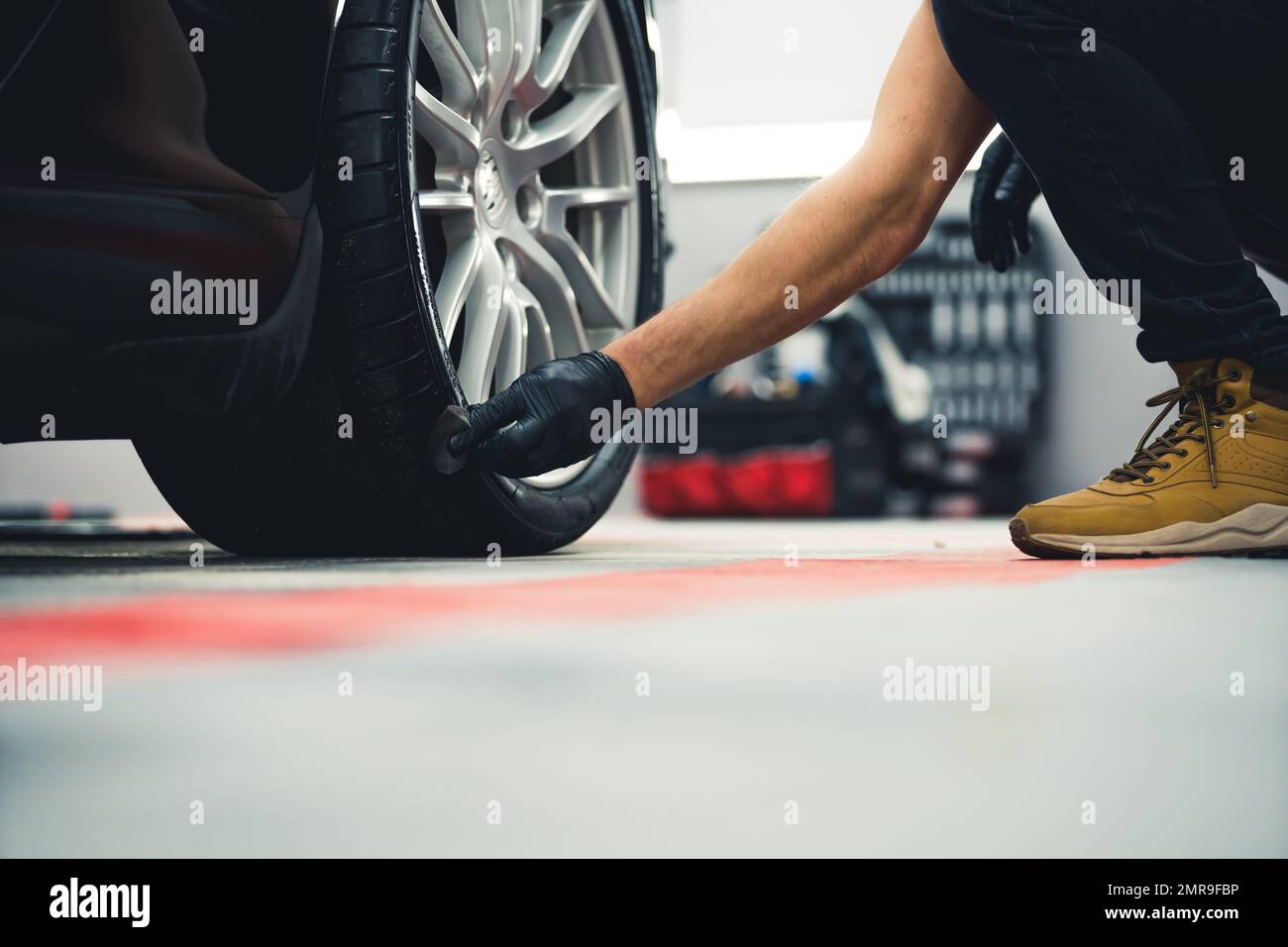 Noircissement des pneus. Homme méconnaissable en gants noirs noircissant les pneus de la voiture à l'aide d'une éponge. Perspective à faible angle. Photo de haute qualité Banque D'Images