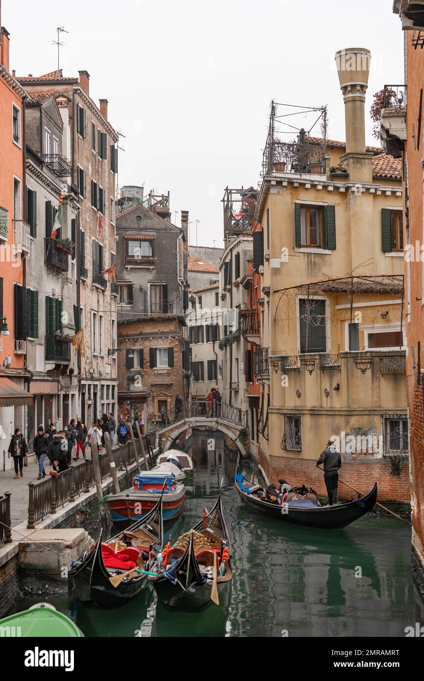 Scène du canal de Venise représentant de petits bateaux et des gondoles dans un quartier résidentiel de Venise en hiver, par une journée gris fraîche avec un peuple dans la rue Banque D'Images